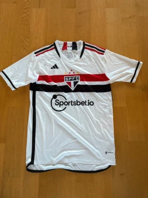 São Paulo FC matchtröja – storlek M - Vit hemmatröja från São Paulo FC (SPFC) från säsongen 2024/25. Storlek M, aldrig använd, nyskick utan lappar. Perfekt för både match, träning eller vardagsbruk. Nypris 699.