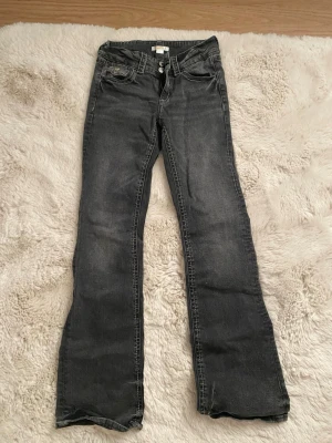 Svarta bootcut jeans från Gina Tricot - Snygga svarta jeans från Gina Tricot i bootcut-modell. Jeansen har klassisk femficksdesign, dubbla silverfärgade knappar och dragkedja framtill. Materialet är jeans med en mörk tvätt och raka ben som breddas nedtill. 