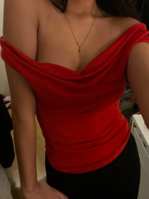 Röd offshoulder topp i sammet - Säljer en snygg röd offshoulder topp i mjuk sammet. Toppen har en draperad halsringning och sitter tight mot kroppen. Perfekt för dig som vill sticka ut med en färgstark och trendig look.