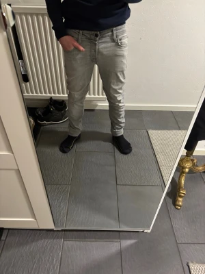 Grå slim jeans storlek 30/32 - Snygga grå jeans i slim fit med klassisk femficksdesign och dragkedja. Jeansen har en modern, smal passform och är tillverkade i mjukt bomullsmaterial med lite stretch för extra komfort. Perfekt för dig som gillar en stilren look.