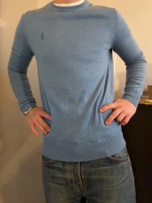 Blå merinoulltröja från Polo Ralph Lauren - Slim fit blå tröja från Polo Ralph Lauren i mjuk och tvättbar merinoull. Klassisk rund hals och långärmad modell med diskret broderad logga på bröstet. Perfekt för dig som gillar stilrena och bekväma plagg med lite lyxig känsla.