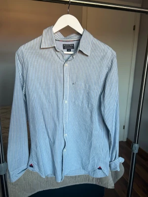 Randig skjorta från Polo Ralph Lauren - Snygg skjorta från Polo Ralph Lauren i ljusblått och vitt med vertikala ränder. Klassisk krage, bröstficka och knappar framtill. Långärmad och tillverkad i mjuk bomull, perfekt för en chill och stilren look.