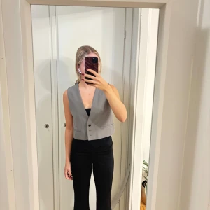Grå kostymväst från Zara - Snygg grå väst från Zara i kostymstil med tre knappar framtill och två fejkade fickor. Strl s. Västen har en rak, croppad passform. Aldrig använd 
