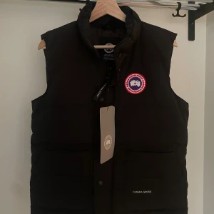 Svart dunväst från Canada Goose - Svart  Canada Goose väst med 2 fickor med mindra fack i. Storlek Medium. Helt ny med tags.(pris går att diskutera)