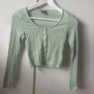 Ljusgrön ribbad topp från Monki - Superfin ljusgrön ribbad topp från Monki i storlek XXS. Modellen är croppad med långa ärmar, rund halsringning och knappar framtill. Den är använd 1 gång och skulle säga att den passar en Xs också😊