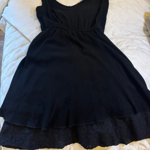 Svart Trendyol klänning med knytband - Supersöt svart klänning från Trendyol med v-ringning och knytbara axelband. Klänningen har en luftig passform och broderad volangkant nertill som ger en extra detalj. Perfekt för varma dagar och enkel att styla med sneakers eller sandaler.