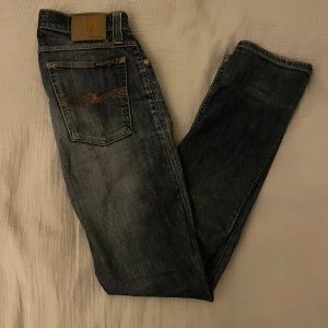 Mörkblå urtvättade Nudie jeans - Snygga jeans från Nudie i klassisk mörkblå urtvättad färg. Riktigt bra passform och tidlös stil som funkar till allt – både vardag och fest. Byxorna har ett hål på knät som ingår i modellen  📏 Storlek: W27 L32 ✨ Skick: Mycket bra skick, sparsamt använda. 🧵 Material: Bomull med stretch för bekväm passform. ✅ Pris kan diskuteras