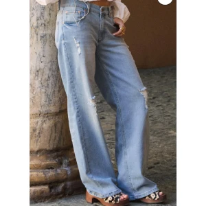 Nelly jeans med hål  - Säljer ett par nelly jeans med slitna detaljer och hål på benen. Jeansen har låg midja och en wide passform med raka, vida ben. Använd några gånger men inget som syns på jeansen.  