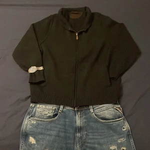 Mörkgrå stickad kofta från März - Mörkgrå merinoull kofta från März Classic i storlek M. Koftan har hel dragkedja framtill, ribbade muddar och krage. Perfekt för lager-på-lager och chill höst- eller vinterstil. Enkel och stilren design med diskret logga på sidan.