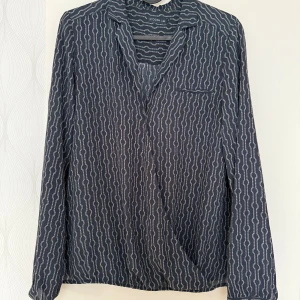 Mönstrad blå skjorta från Stockh LM - Snygg blå skjorta från Stockh LM med unikt geometriskt mönster i vitt. Skjortan har lång ärm med knapp vid manschetten, klassisk krage och en bröstficka. Materialet är mjukt och lätt, perfekt för dig som gillar stilrena detaljer.