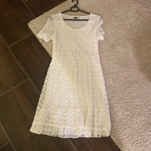 Vit spetsklänning från Isolde - Superfin vit student tklänning från Isolde med spets över hela klänningen  och ett skirt plisserat lager längst ner. Klänningen har rund halsringning, korta ärmar och ett feminint, luftigt fall. St S passar även m om man vill.