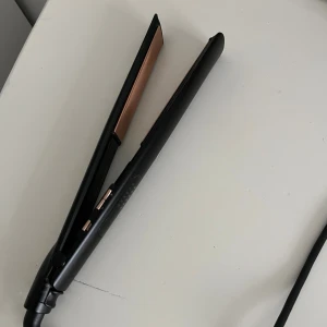 Plattång - Elegant svart plattång med keramiska plattor i kopparfärg. Produkten ser ut att vara i gott skick utan synligt slitage eller defekter. Perfekt för att skapa släta och glansiga frisyrer. Enkel att använda med smidig sladd och värmereglering.