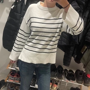 Vit randig stickad tröja med slit - Säljer en vit stickad tröja med svarta horisontella ränder och breda ribbade muddar vid ärmslut och nederkant. Storleken är xs-s Tröjan har rund hals och slits på sidorna. Perfekt att matcha med jeans eller till hösten💕