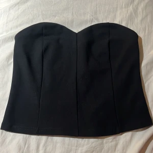 Svart tubtopp  - Säljer en svart tubtopp  i storlek L. Toppen har en bandeauformad överdel och smockad baksida för extra komfort. Enkel och stilren design som sitter snyggt på kroppen. Perfekt att matcha med jeans eller kjol.
