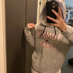 Grå hoodie Tommy Jeans med huva - Säljer nu min snygga gråa hoodie från Tommy Hilfiger. Nypris 1000 men säljer för 499. Tröjan är nyskick endast använd 1-2 gånger. Tröjan har huva med svarta snören, magficka och långa ärmar. Perfekt nu till hösten med jeans eller mjukisar!!🌸