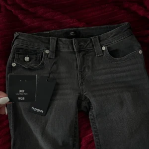 True Religion Joey Low Rise Flare jeans - PRIS KAN DISKUTERAS -Snygga mörkgrå jeans från True Religion, modell Joey Low Rise Flare. De har låg midja, bootcut-ben och coola detaljer som silverfärgade knappar och fickor med lock bak. Jeansen är gjorda i klassiskt jeansmaterial och har en stilren, modern look.