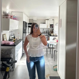 Vit blus med spets från Lindex🤍 - Säljer en söt vit blus från Lindex i storlek 40. Blusen är ärmlös med rund halsringning, spetsdetaljer och broderade partier framtill. Den har en lätt volang nertill🤍