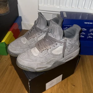 Nike Air Jordan 4 x KAWS grå mocka - Nike Air Jordan 4 x KAWS sneakers i helgrå mocka med ikoniska KAWS-detaljer och broderade XX på hälen. Skorna har snörning, platt sula och rund tå. Perfekta för dig som vill sticka ut med en unik sneaker.