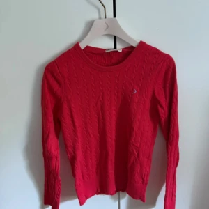 Röd kabelstickad tröja Boomerang - Snygg röd kabelstickad tröja från Boomerang med rund halsringning och diskret logga på bröstet. 💕