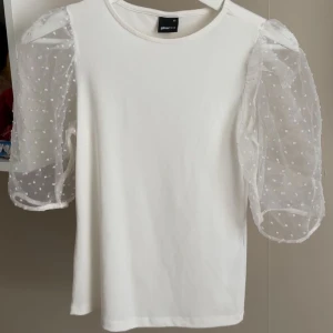 Vit topp med puffärmar från Gina Tricot - Supersöt vit topp från Gina Tricot med transparenta puffärmar i mesh och små prickar. Kroppen är i mjuk bomull och ärmarna ger en extra touch. Perfekt för dig som vill sticka ut lite extra med detaljerade ärmar.