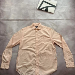 Ljusrosa skjorta från Ralph Lauren - Snygg ljusrosa skjorta från Ralph Lauren med klassisk krage och knappar hela vägen. Skjortan är långärmad och har en stilren, enkel design utan mönster. Tillverkad i mjuk bomull som känns skön mot huden. Perfekt för dig som gillar clean och fräsch stil.