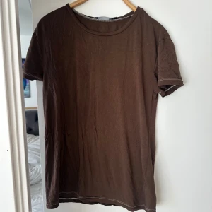 Brun t-shirt från 157, storlek M - En basic brun t-shirt från 157 i storlek M. T-shirten har rund halsringning, korta ärmar och är tillverkad i mjuk viskosmix med lite stretch för skön passform. Perfekt till jeans eller shorts för en chill look. Finns ett litet hål på ena skulderbladet se bild