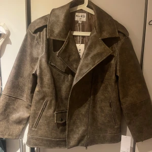 Brun bikerjacka  - Säljer en brun bikerjacka från NA-KD i PU-material med cool washed out-effekt. Jackan har bred krage, sned dragkedja, flera fickor med dragkedja och en liten ficka med knapp. Den är helt ny med prislapp kvar i storlek 36. Nypris 1099 säljer för 750 men pris kan diskuteras 