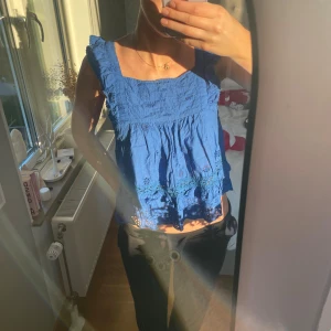 Blå blus med volang och broderi - Säljer en blå blus med fyrkantig halsringning och volangdetaljer vid axlarna. 