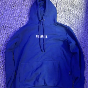 Blå mjukis set från Hoodrich - Säljer ett par blå mjukisbyxor från Hoodrich med vit logga tryckt på ena benet. Byxorna har dragsko i midjan och smal passform med muddar vid bensluten. Perfekta för chill eller streetwear-stil.