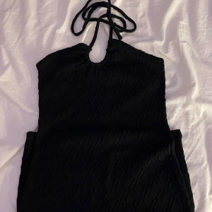 Svart halterneckklänning H&M Divided - Svart kort halterneckklänning från H&M Divided i storlek S. Klänningen har knytband i nacken och ett diskret strukturmönster i tyget. Snygg och enkel modell som sitter tajt upptill och har en rak passform.