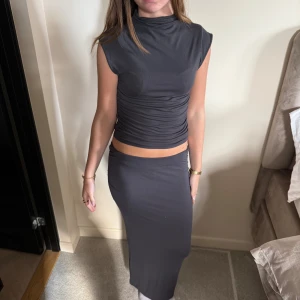 Mörkgrå långkjol i mjukt material - Säljer en stilren mörkgrå långkjol med rak passform. Kjolen är enkel och har en slät yta utan mönster eller detaljer, vilket gör den lätt att matcha med olika toppar. Materialet känns mjukt och stretchigt, perfekt för en chill och snygg look.