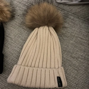 Beige ribbstickad mössa Hollies - Beige aktig mössa från Hollies, äkta päls. Använd max 3 gånger