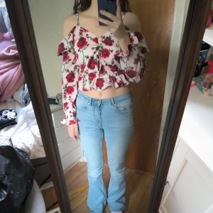 Blommig croppad topp från H&M Divided - Supersöt croppad blus från H&M Divided med rödblommigt mönster på vit botten. Toppen har offshoulder-modell med volangdetaljer, långa ärmar och knyt framtill. Perfekt för vår och sommar när du vill sticka ut lite extra. Knappt använd.