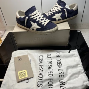 Golden Goose Superstar blå sneakers - Golden Goose Superstar sneakers i marinblå mocka.  Skorna är lite skavda i häl (normalt på dessa skor) nu pris är över 6000kr så tänk på det innan ni lägger skambud. Kartong,Dustbag och äkthetsbevis ingår. Hör gärna av dig vid frågor.
