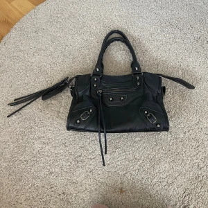 Svart Balenciaga liknande väska - Köpt för drygt 1 år sen, finns tecken på användning då den är lite sliten på lädret på vissa ställen, men inget som syns tydligt! Köpt för 1000 kr. Axelband tillkommer.