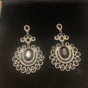 Silver örhängen med svarta stenar - Snygga och detaljerade örhängen silver med svarta, facetterade stenar. De har en oval form med droppformade detaljer runt om och ett elegant, vintageinspirerat mönster. Perfekta för dig som vill sticka ut med ett statement-smycke.🖤Vad är den svarta stenens energi? Den symboliserar ursprunglig renhet, förnyelse av förbund och skingrar negativitet.🖤🖤