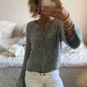 Grå stickad kofta med pärlknappar - Mysig grå stickad kofta. Koftan har pärlknappar framtill och är tillverkad i ett fluffigt material som känns extra skönt mot huden. Perfekt för dig som gillar chill och trendiga vibes.