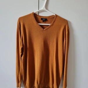 V-ringad tröja från SMOG (New Yorker) strl M - Säljer en ockra färgad v-ringad tröja från SMOG (New Yorker) i regular fit. Tröjan har långa ärmar och ribbade muddar vid hals, ärmslut och nederkant. Material bomull och polyester. Storlek M.