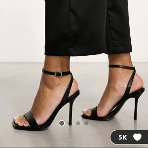 Svarta klackskor  - Stilrena svarta sandaler med smal rem runt vristen och öppen tå. Skorna har hög smal klack och en minimalistisk design med tunna remmar i syntetmaterial. Perfekta för dig som vill ha en clean och elegant look. Aldrig använda och säljs här för att jag inte hann skicka tillbaka de!!