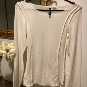 Vit långärmad topp från Chiquelle - Säljer en stilren vit långärmad topp från Chiquelle. Toppen har en rund halsringning och dekorativa sömmar längs framsidan som ger en cool detalj. Materialet är mjukt och lätt, perfekt för lager-på-lager eller som den är. 