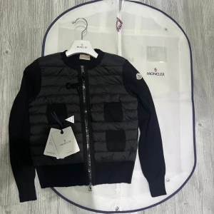 Moncler cardigan dam - Hej! En Moncler cardigan för dam till salu. Jackan är i jättefint skick och har inga defekter eller liknande. Den är äkta och köpt online  kvittot finns. Jag säljer den pågrund av att den inte riktigt passar min stil. Den är jättefin och jag fick alltid jätte många komplimanger när jag andvände den. Moncler dustbag lapprna osv ingår med jackan. Hör av dig vid minsta lilla fråga! 💕