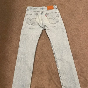 Levi's 501 ljusblå jeans W29 L32 - Säljer ett par klassiska Levi's 501 Premium jeans i ljusblå tvätt. De har raka ben, hög midja och knäppning med knappar. Ikonisk läderpatch bak och femficksmodell. Perfekta för dig som gillar vintagevibbar och tidlös stil. Väldigt bra skick