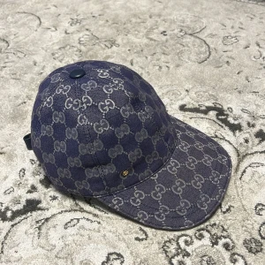 Gucci blå keps med GG-mönster - Snygg blå keps från Gucci med klassiskt GG-monogram i grått över hela kepsen. Justerbar rem baktill med läderdetalj och metallspänne. Kepsen är tillverkad i bomull och har en rundad form med böjd skärm. Perfekt för dig som vill ha en lyxig streetstyle-look.