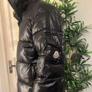 Moncler Maya - Monclear Maya som jag köpt här på plick, säljer på grund av att den var för stor på mig. Jackan är svart och perfekt för vintern. Tre fickor på utsidan samt en på insidan. Jackan har luva och är i glansigt material. Jackan har tre hål, två små på utsidan av jackan (bild 4) och ett större hål under ena armhålan (bild 5), tråden har gått upp lite på serieteckningen samt små fläckar bredvid serieteckningen på insidan av jackan. Pris kan absolut diskuteras, skriv om ni vill ha fler bilder på jackan!