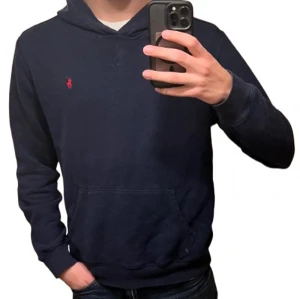 Marinblå hoodie från Polo Ralph Lauren - Snygg marinblå hoodie från Polo Ralph Lauren med röd logga på bröstet. Bra skick, men använd. Storlek M som passar mig ca 185 cm lång.