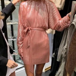 Adoore klänning - Supersnygg rosa kortklänning med shimrigt tyg och plisserade detaljer. Klänningen har långa, vida ärmar och ett matchande bälte i midjan som knyts. Den har ett randigt mönster och ger en riktigt trendig vibe. Perfekt för dig som vill sticka ut och glänsa💕