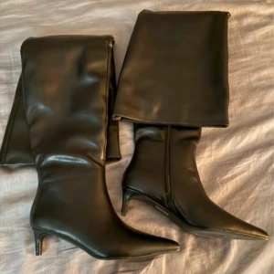 Svarta overknee stövlar från Nelly - Säljer ett par svarta overknee stövlar från Nelly med spetsig tå och låg klack. Stövlarna är i syntetmaterial med en glansig finish och har dragkedja på insidan. Perfekta för att lyfta vilken outfit som helst. Nypris 1100kr klacken är 5cm