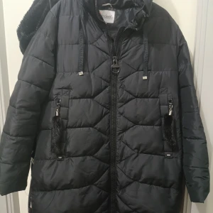 Svart quiltad pufferjacka Visdeer - Svart pufferjacka från Visdeer med huva och snygga snören. Jackan har quiltad design, dragkedja framtill och två fickor med dekorativa svarta pälsdetaljer. Perfekt för kalla dagar och har en loose passform som ger skön streetkänsla.