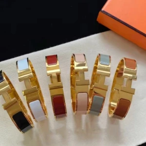  H-armband i olika färger - Säljer flera ikoniska  H-armband i guldpläterad metall med emaljdetaljer. Finns i svart, vit, röd, rosa, gråblå och orange. Snyggt H-spänne framtill och stilren design som lyfter din outfit. Perfekt accessoar för dig som gillar lyx och färg.
