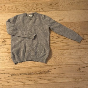 Grå stickad tröja från Garde Grisch - Mysig grå stickad tröja från Garde Grisch i storlek XS. Tröjan har rund hals och långa ärmar med ribbade muddar vid hals, ärmslut och nederkant. Perfekt för dig som gillar enkel och stilren design med en soft vibe.